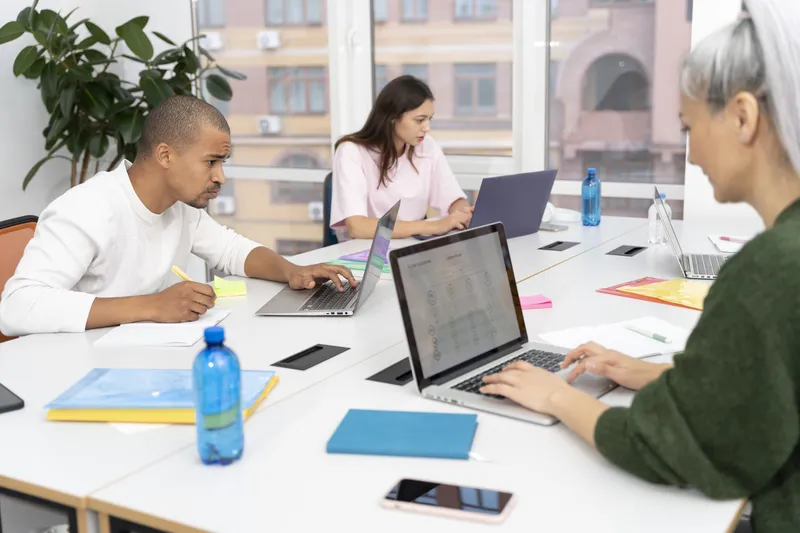 Colleagues work together around laptops at a bright shared office table